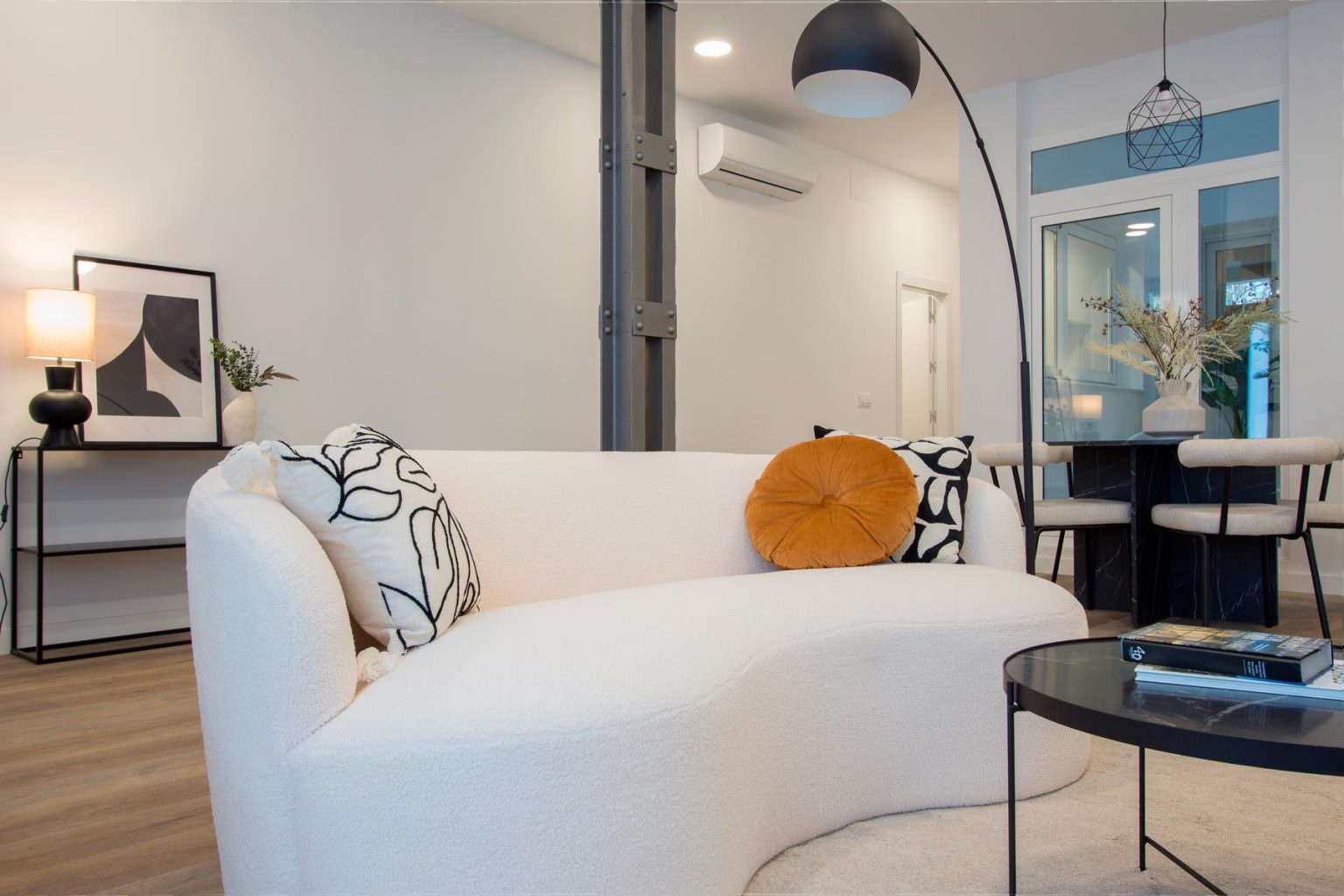 Interiorismo de salón moderno con sofá blanco curvo, mobiliario de diseño, iluminación decorativa y comedor integrado | Realzo